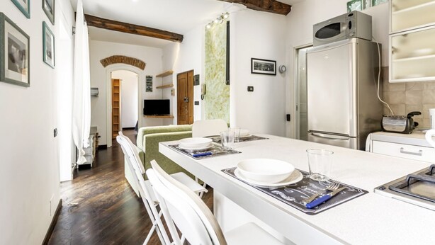 Una cocina moderna con una isla central, muebles blancos y un refrigerador de acero inoxidable.