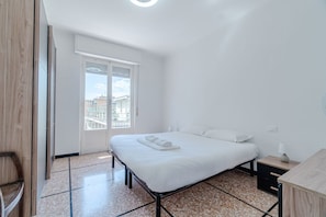 A bedroom with a bed, a nightstand, a window, and a view of buildings.