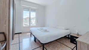 A bedroom with a bed, a nightstand, a window, and a view of buildings. - GuestHost - Cozy and bright 80 sqm apartment, perfect for 5 people, located on the second floor of a building with a lift.Located in the heart of the Ligurian Riviera, the property is located in Rapallo, in a convenient and well-served area. The location (Rapallo)