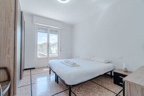 A bedroom with a bed, a nightstand, a window, and a view of buildings. - GuestHost - Cozy and bright 80 sqm apartment, perfect for 5 people, located on the second floor of a building with a lift.Located in the heart of the Ligurian Riviera, the property is located in Rapallo, in a convenient and well-served area. The location (Rapallo)