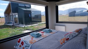 Un dormitorio con cama, ventana y vista a un edificio y montañas.