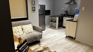 Un espacio habitable compacto con sofá, una pequeña cocina que incluye refrigerador y microondas, y un armario de madera.