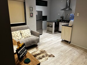 Una sala moderna con un sofá gris, una alfombra pequeña y un cartel de bienvenida.