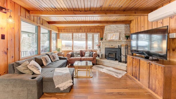 A cozy cabin interior with a stone fireplace, wooden walls, and a large TV.