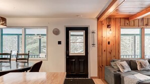 A cozy room with a wooden floor, a dining table with chairs, a sofa with cushions, and a door with a coat rack.