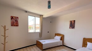 Une pièce comprenant deux lits en bois, un porte-manteau en bois, une fenêtre avec des rideaux et deux tableaux accrochés au mur.