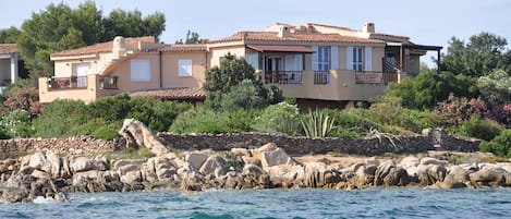 A coastal villa with a stone wall and balcony overlooking the sea.