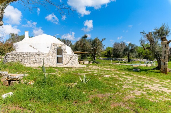A white dome-shaped building with a stone exterior, surrounded by greenery and trees. - Trullo Mandorlo by Wonderful Italy (Carovigno)