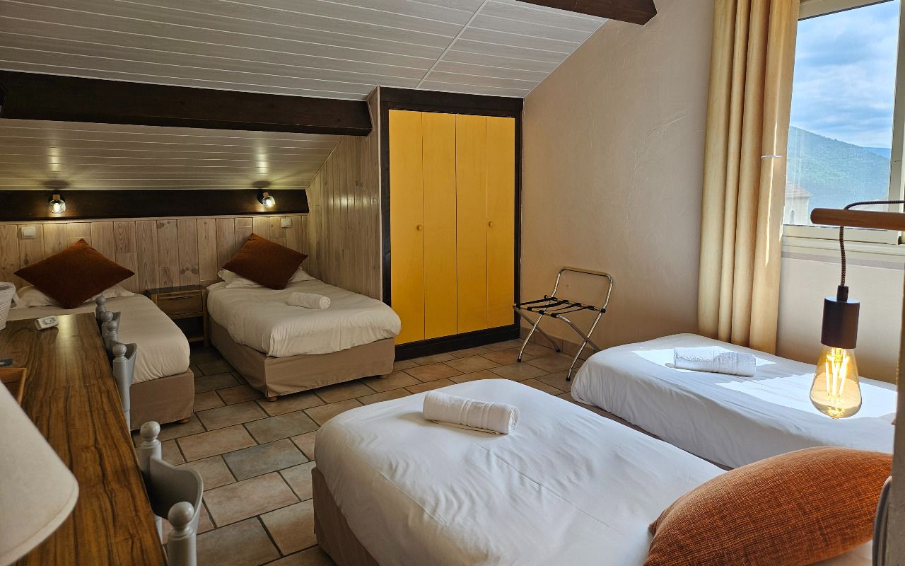 Habitación de hotel con dos camas, un cabecero de madera, un armario amarillo, una ventana con vistas y una bombilla colgante.