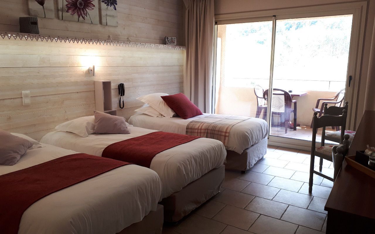 Una habitación de hotel con dos camas, una puerta corrediza al balcón y un cabecero de madera.