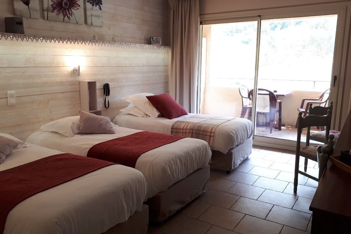 A hotel room with two beds, a sliding glass door to the balcony, and a wooden headboard.