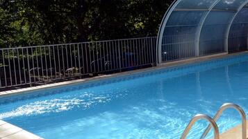 Une piscine à l’eau d’un bleu cristallin, entourée d’une clôture métallique et d’une structure en verre formant une serre.