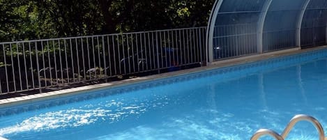 A swimming pool with a clear blue water surface, surrounded by a metal fence and a glass greenhouse structure.
