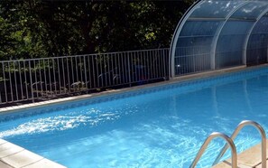 A swimming pool with a clear blue water surface, surrounded by a metal fence and a glass greenhouse structure. - Logis Hotel Le Mont Barral (Châtillon-en-Diois)