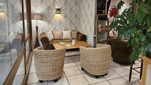 A cozy room with a brown sofa, two wicker armchairs, a coffee table, and a large green plant. - Logis Hotel Le Mont Barral (Châtillon-en-Diois)
