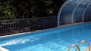 A swimming pool with a clear blue water surface, surrounded by a metal fence and a glass greenhouse structure. - Logis Hotel Le Mont Barral (Châtillon-en-Diois)