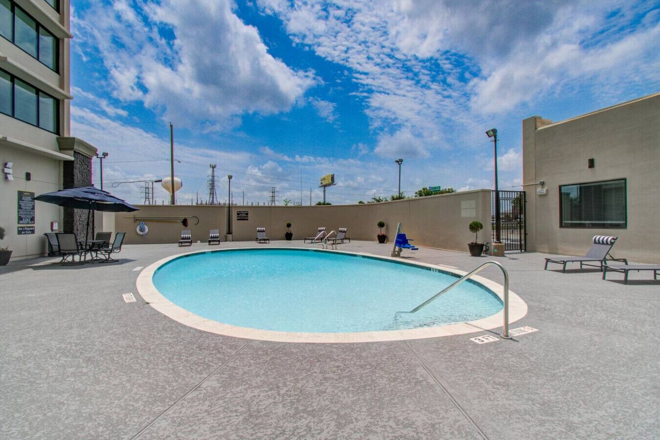 Una piscina con sillas de descanso y sombrillas, rodeada de edificios.