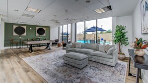 Ein modernes Wohnzimmer mit Blick auf einen Pool, einem Billardtisch und einem großen, grauen Ecksofa.