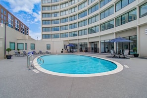 A modern hotel with a central swimming pool, lounge chairs, and outdoor seating areas.