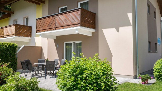 Ein Gebäude mit zwei Balkonen, einer Terrasse mit Gartenmöbeln und gepflegter Bepflanzung.