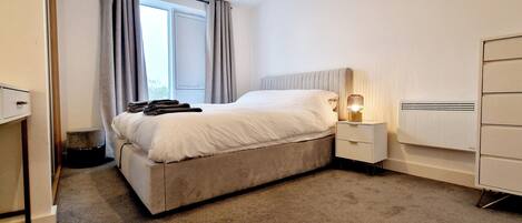 A neatly made bed with a headboard, a bedside lamp, a small bedside table, and a wardrobe.