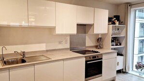 Une cuisine moderne avec des meubles blancs, un évier en acier inoxydable et un four.