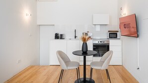 Une cuisine moderne avec des meubles blancs, une table à manger avec deux chaises, un vase de fleurs séchées et un panneau indiquant « PRÊT POUR LES INVITÉS » accroché au mur.