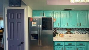 Une cuisine avec des armoires de couleur turquoise, un réfrigérateur en acier inoxydable et un plafond en bois.