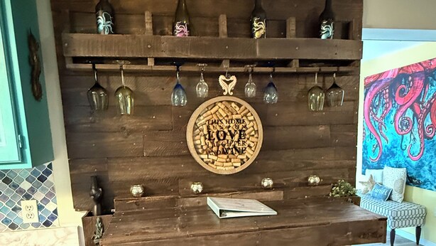 Une cuisine avec un mur en bois, deux tabourets et un meuble à vin contenant des bouteilles et des verres.