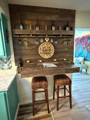 Une cuisine avec un mur en bois, deux tabourets et un meuble à vin contenant des bouteilles et des verres.