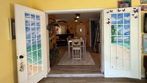 Une pièce avec un plancher en bois, une table à manger avec des chaises, et une vue sur un espace de vie comprenant un canapé et une guitare.