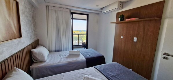 Habitación de hotel con dos camas, un ventanal con vistas, una puerta de madera y un equipo de aire acondicionado.
