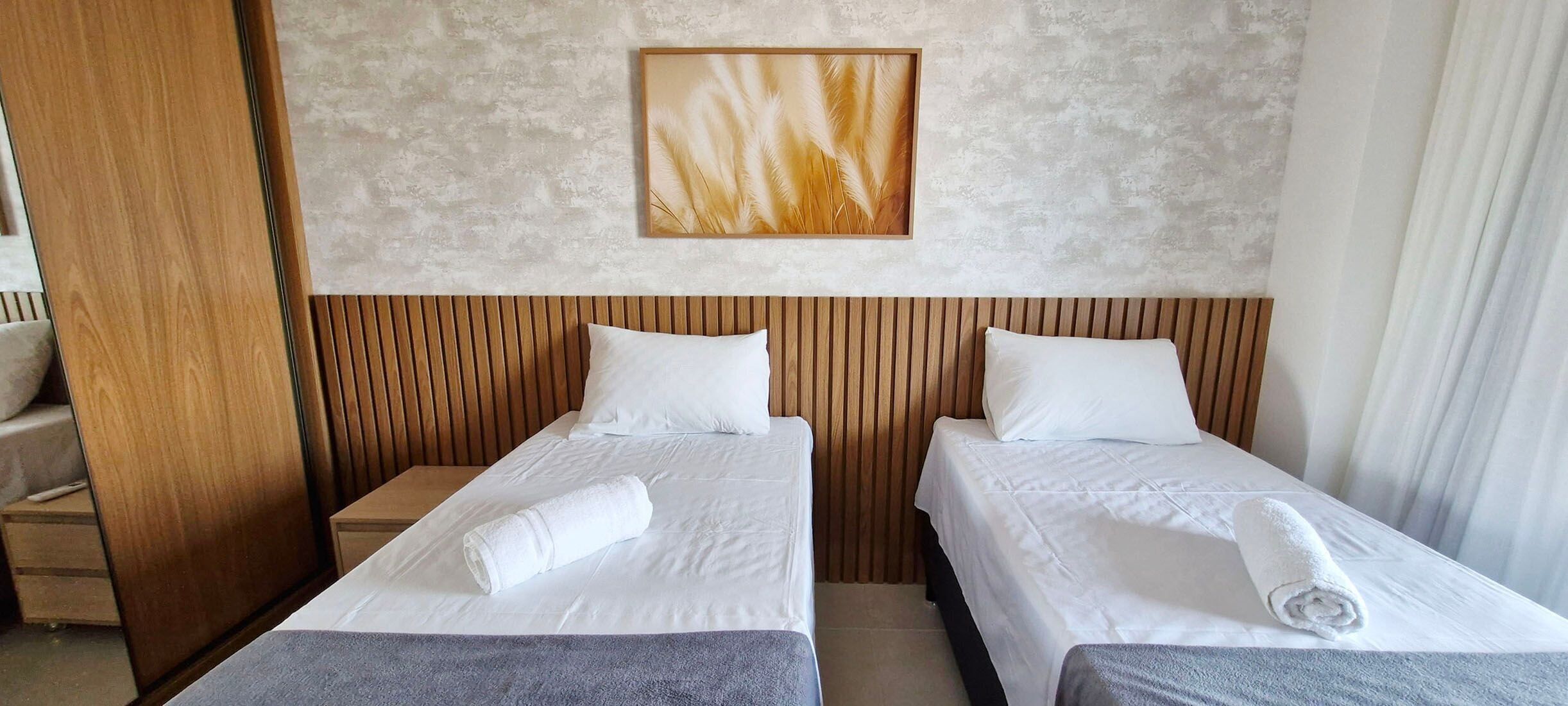 A hotel room with two single beds, wooden headboards, white bedding, a framed artwork on the wall, and a view of the outdoors.