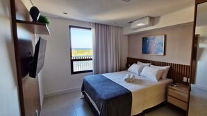A hotel room with a bed, a TV mounted on the wall, a window with a view, a painting on the wall, and a balcony.