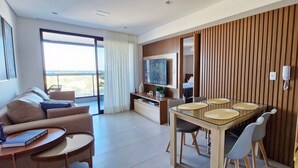 A modern hotel room with a living area, dining space, and a balcony with a view.