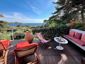 Un terrazzo in legno con mobili da esterno, un vaso grande e una vista panoramica sul mare e le colline.