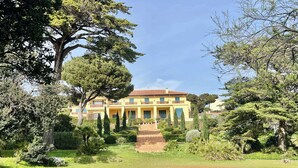 A large yellow building with a red roof, surrounded by lush greenery and a swimming pool. - Villa 5 rooms with pool near the sea (Hyères)