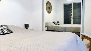 Une chambre à coucher avec un lit, une table de chevet, un miroir et une fenêtre avec des volets.