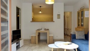 Un espace de vie compact comprenant un téléviseur, une petite table en bois, un canapé bleu et un meuble avec des portes en verre.