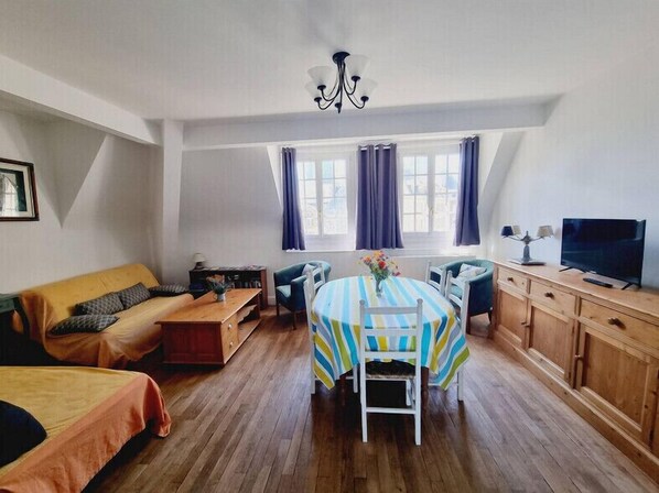 Ein gemütliches Zimmer mit einer Couch, einem Esstisch, einem Fernseher und einem Fenster mit Vorhängen.