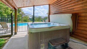 Ein Whirlpool in einer Holzhütte mit Blick auf ein Schwimmbecken und ein Metalltor.