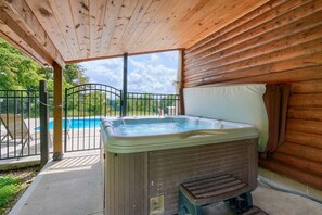 Un jacuzzi en una cabaña de madera con vista a una piscina y una reja de metal.