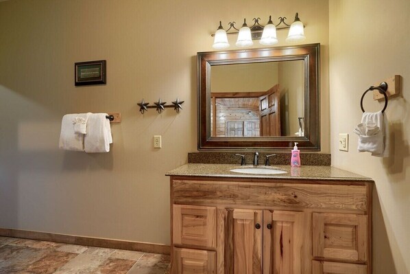 A bathroom with a wooden vanity, a large mirror, and a sink. There are towels hanging on hooks and a framed certificate on the wall. - Timber View | Hocking Hills, Pool, Lodge, Pets (Rockbridge)