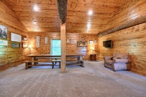 A cozy cabin interior with a wooden ceiling, a large wooden table, a sofa, and framed pictures on the walls.