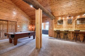 A wooden interior with a pool table, a bar area with stools, and a sign on the wall.