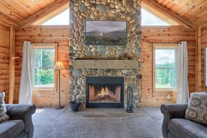 A log cabin interior with a stone fireplace, two windows, and a cozy seating area.