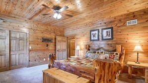 Ein Schlafzimmer in einer Blockhütte mit Bett, Sitzbank, Deckenventilator und gerahmten Bildern an der Wand.