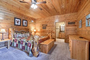 Ein Schlafzimmer in einer Blockhütte mit einem Holzbett, einer Bank, einem Schreibtisch und einem Deckenventilator.