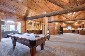 A wooden interior with a pool table, a bar area, and a kitchen.