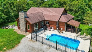 A log cabin with a swimming pool, stone chimney, and outdoor seating area. - Timber View | Hocking Hills, Pool, Lodge, Pets (Rockbridge)